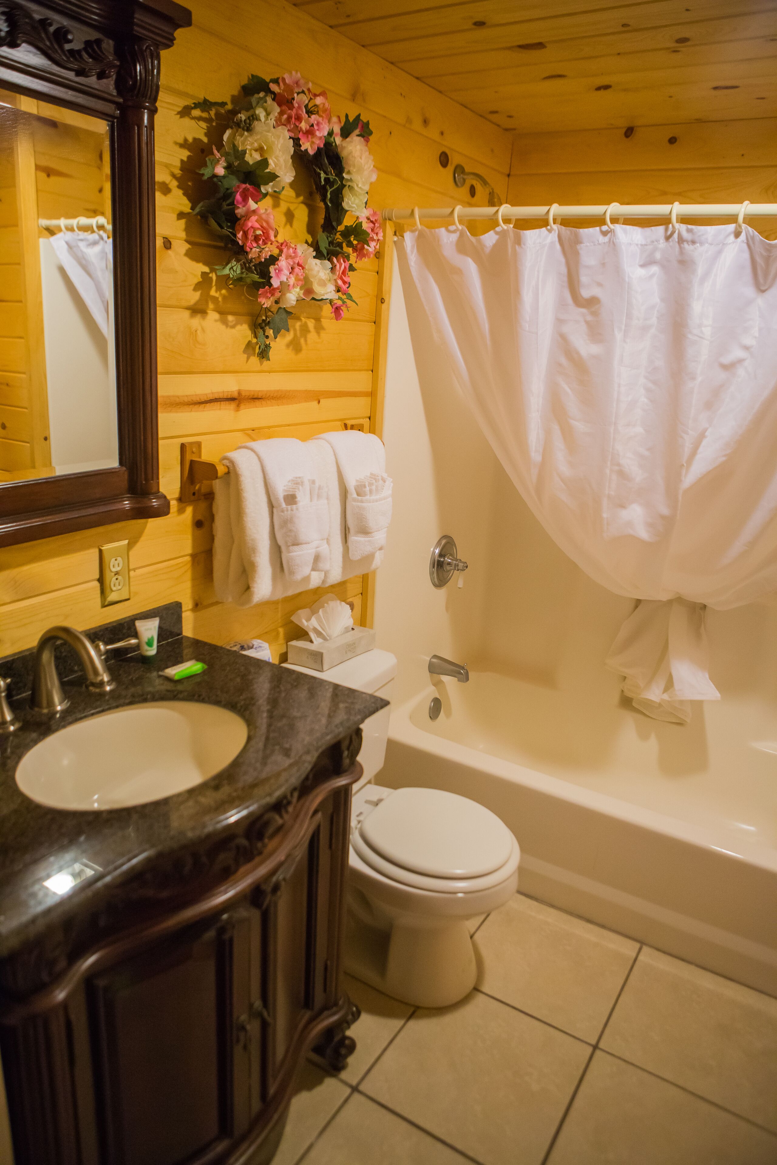 A bathroom with a wooden interior, a sink with a mirror, a toilet, and a bathtub with a shower curtain.