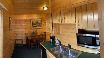 A wooden cabin interior with a dining area, a sink, and a microwave.