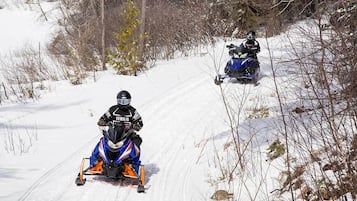 Two snowmobiles on a snowy trail surrounded by trees.