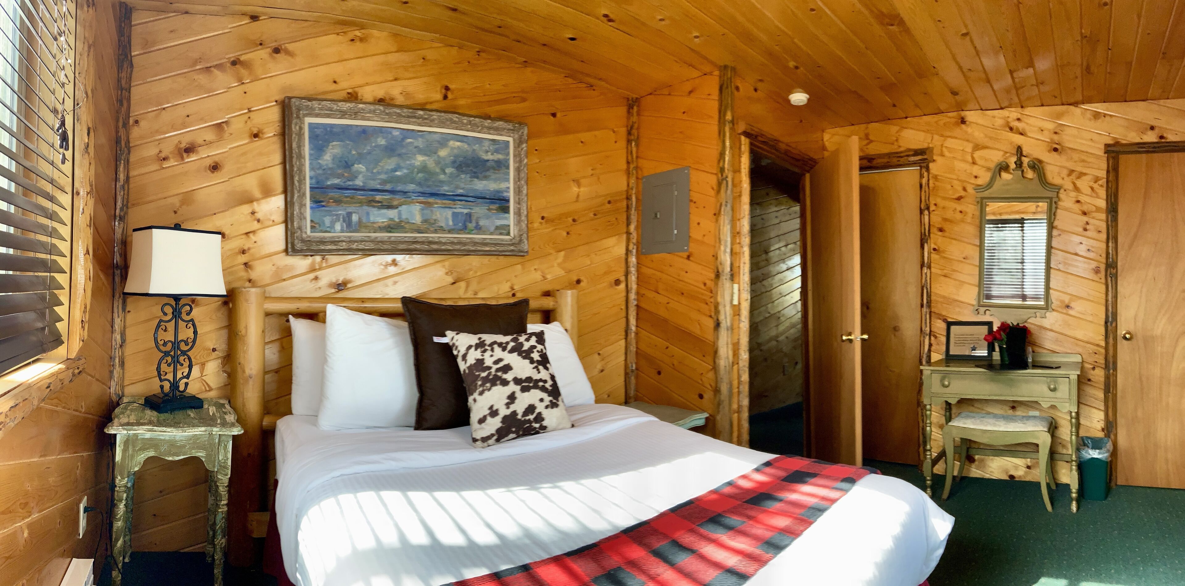 Ein Zimmer in einer Holzhütte mit einem Bett, einem Gemälde, einem Schreibtisch und einem Spiegel.