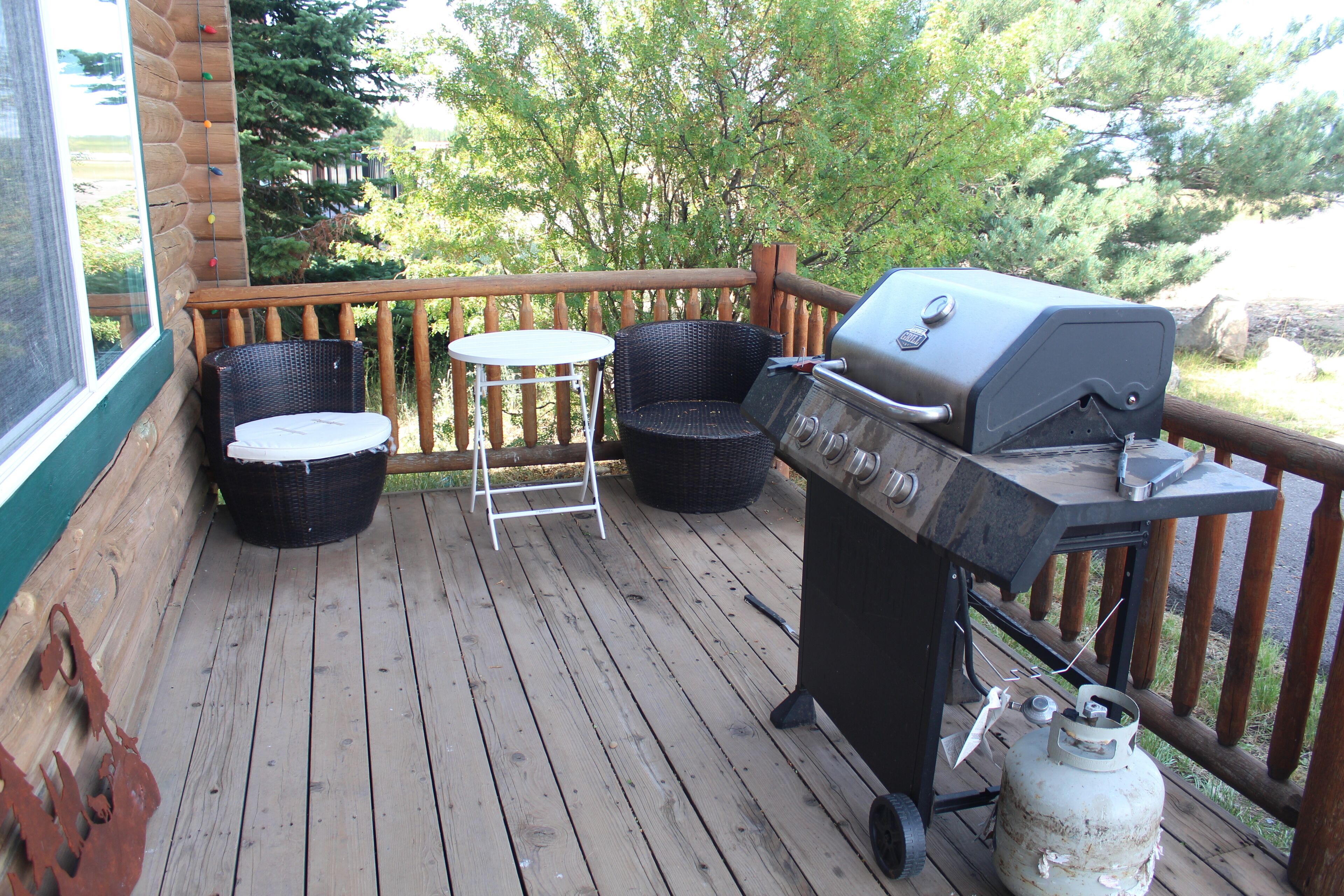 A wooden deck with a grill, two wicker chairs, and a small table.