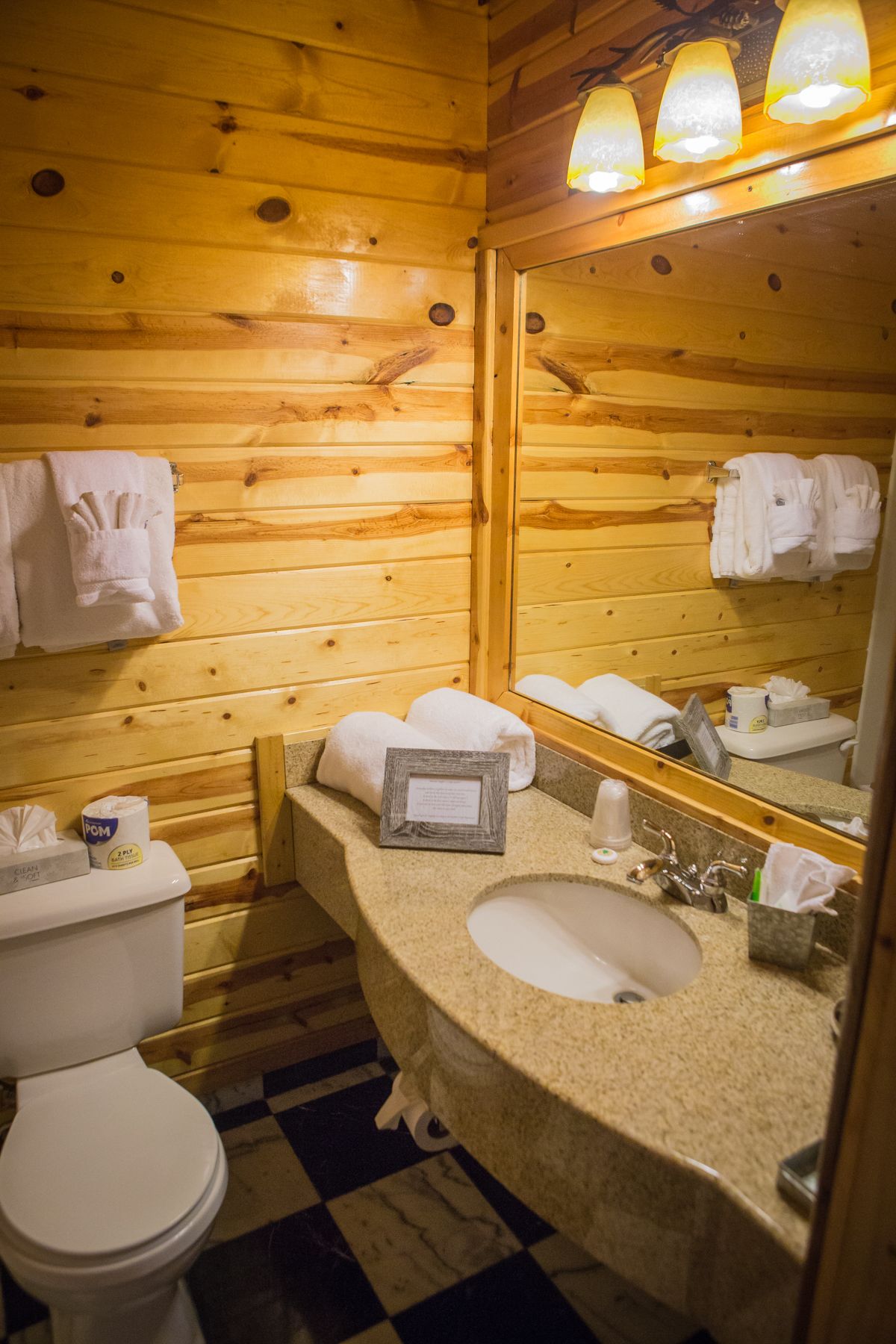 A wooden cabin bathroom with a sink, mirror, and toilet.