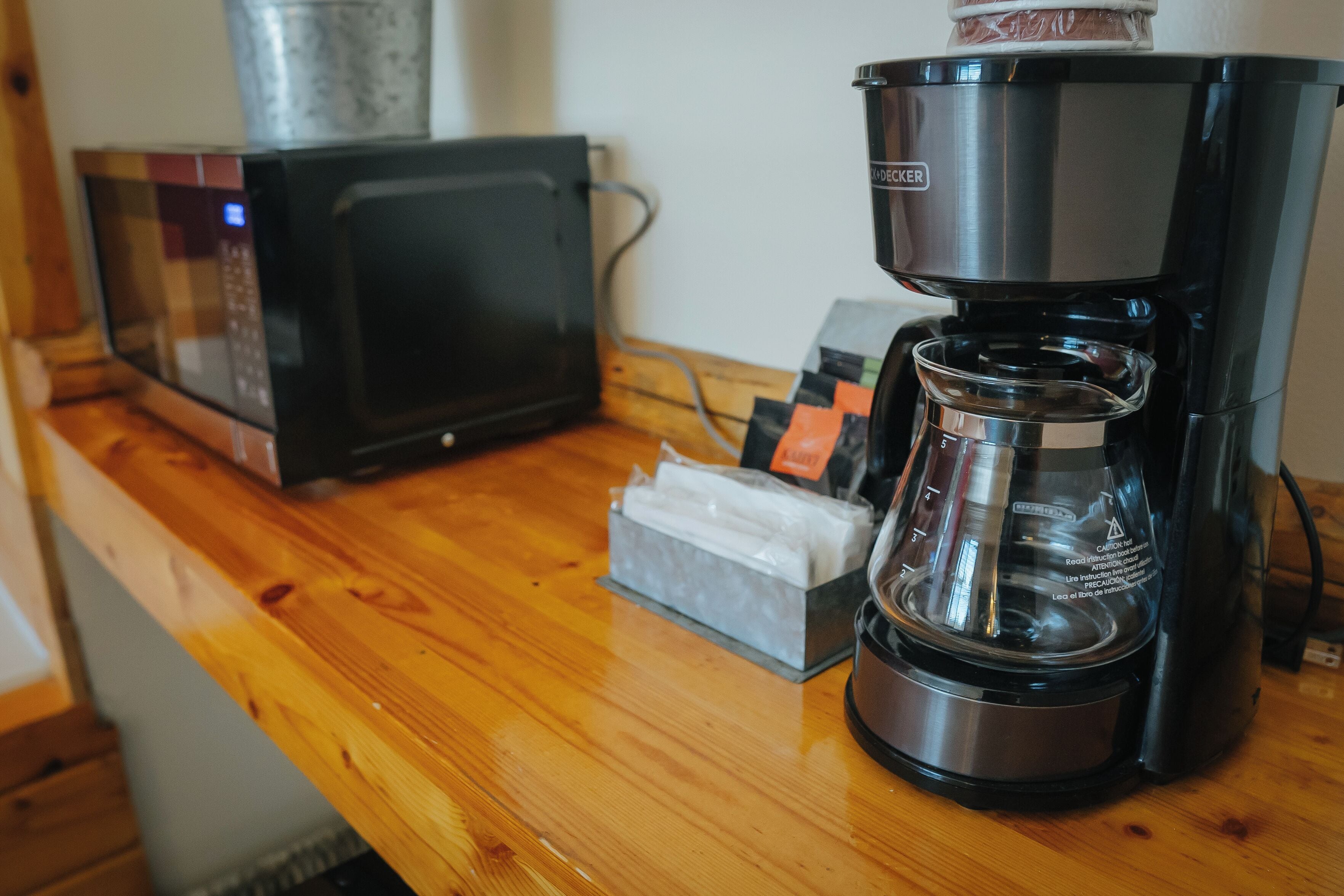 A coffee maker on a wooden countertop with a microwave and a tissue box nearby.