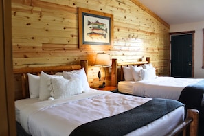 A wooden cabin room with two beds, a framed fish painting, and a door.