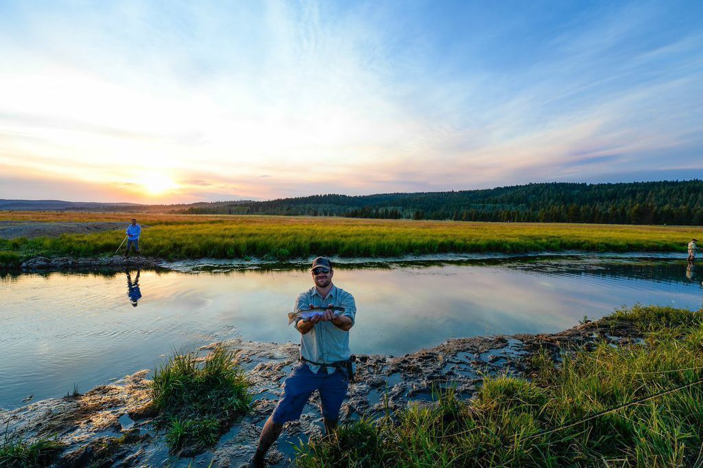 A person standing by a calm river with a sunset in the background.
