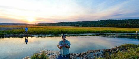 A person standing by a calm river with a sunset in the background.