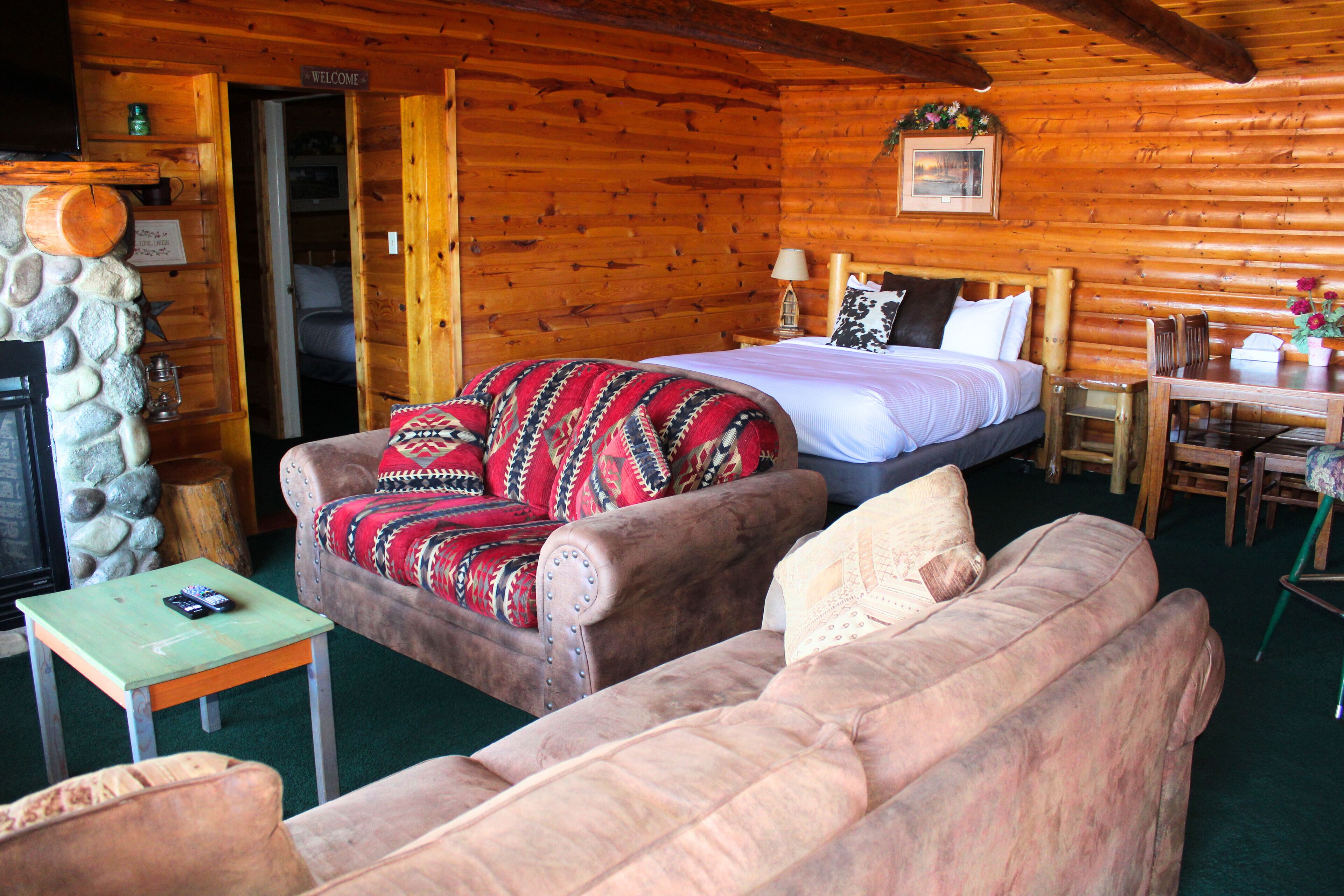 A cozy log cabin room with a bed, two sofas, a small table, and a television.