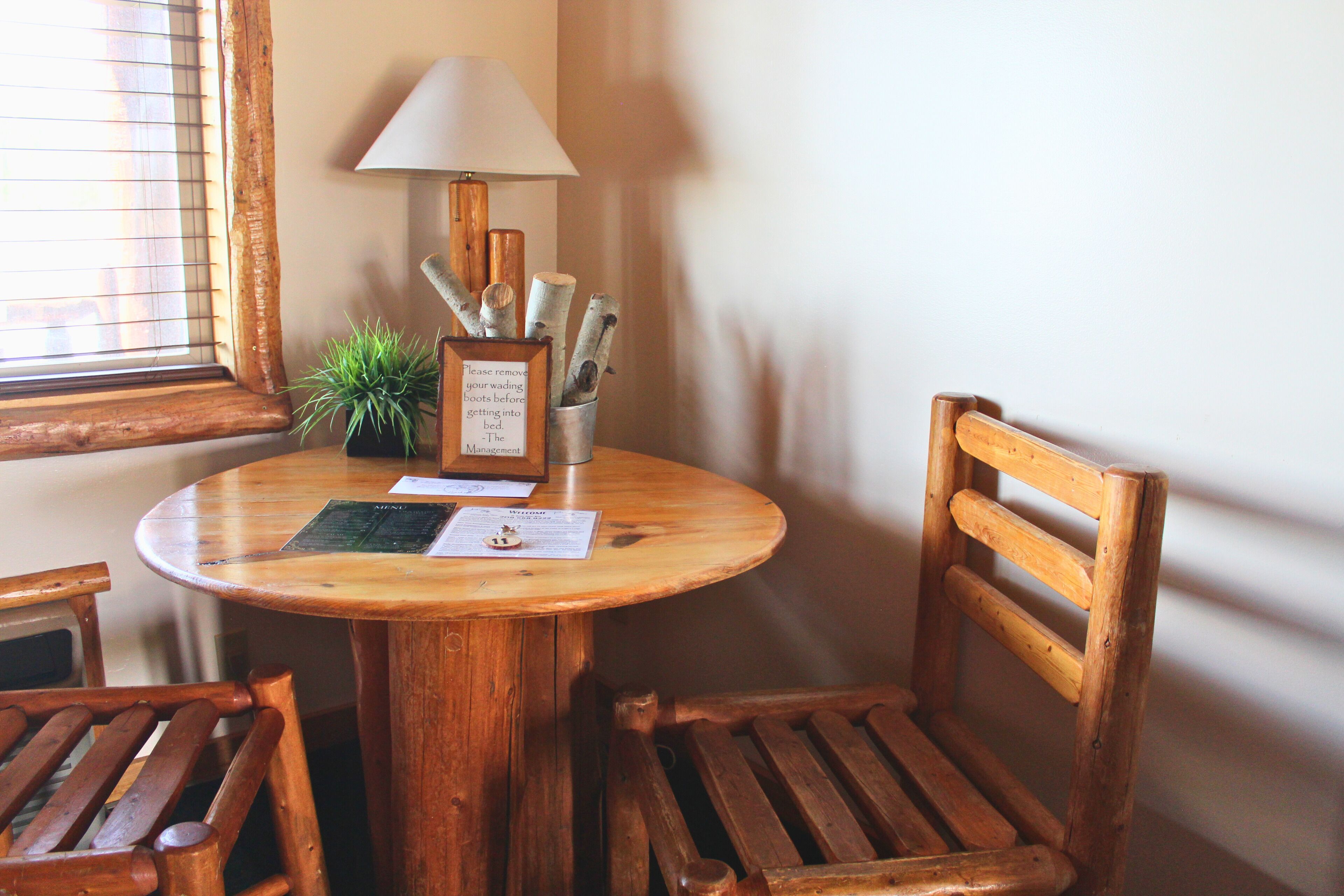 Une table ronde en bois, sur laquelle se trouvent une lampe, un panneau encadré et une plante en pot.
