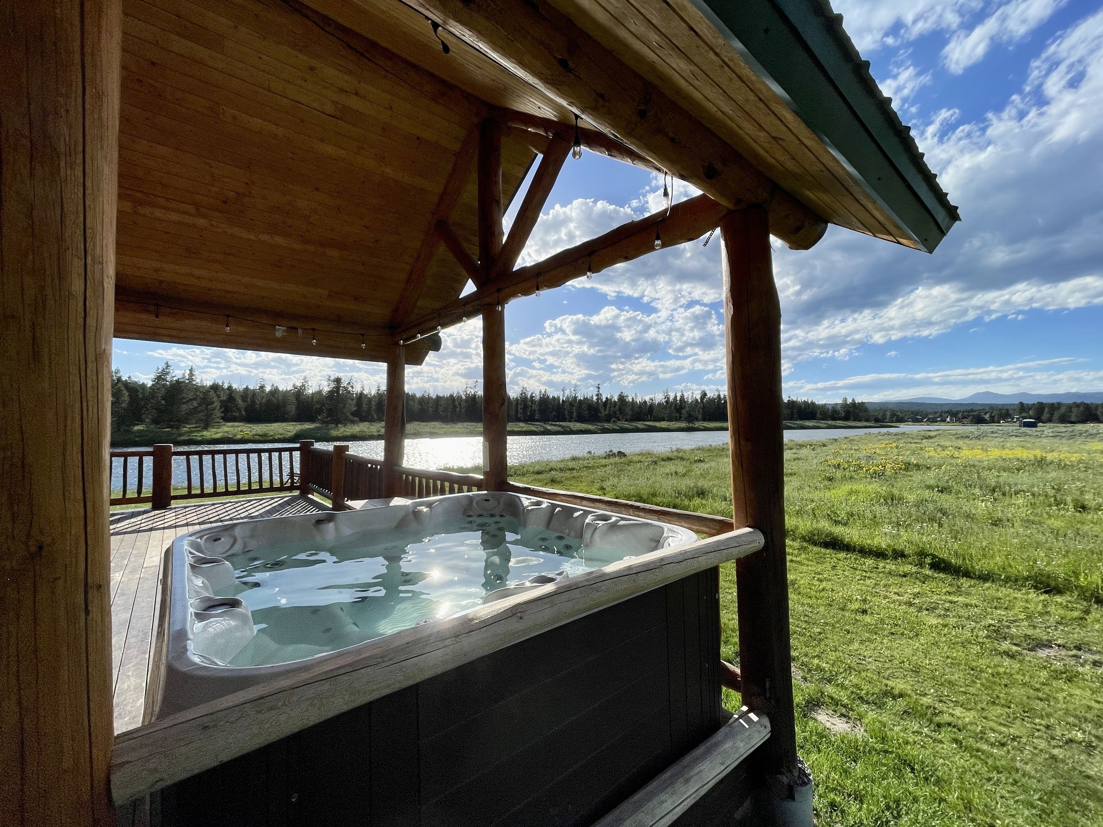 Une cabane en bois dotée d’un bain à remous, avec vue sur un lac et une forêt.