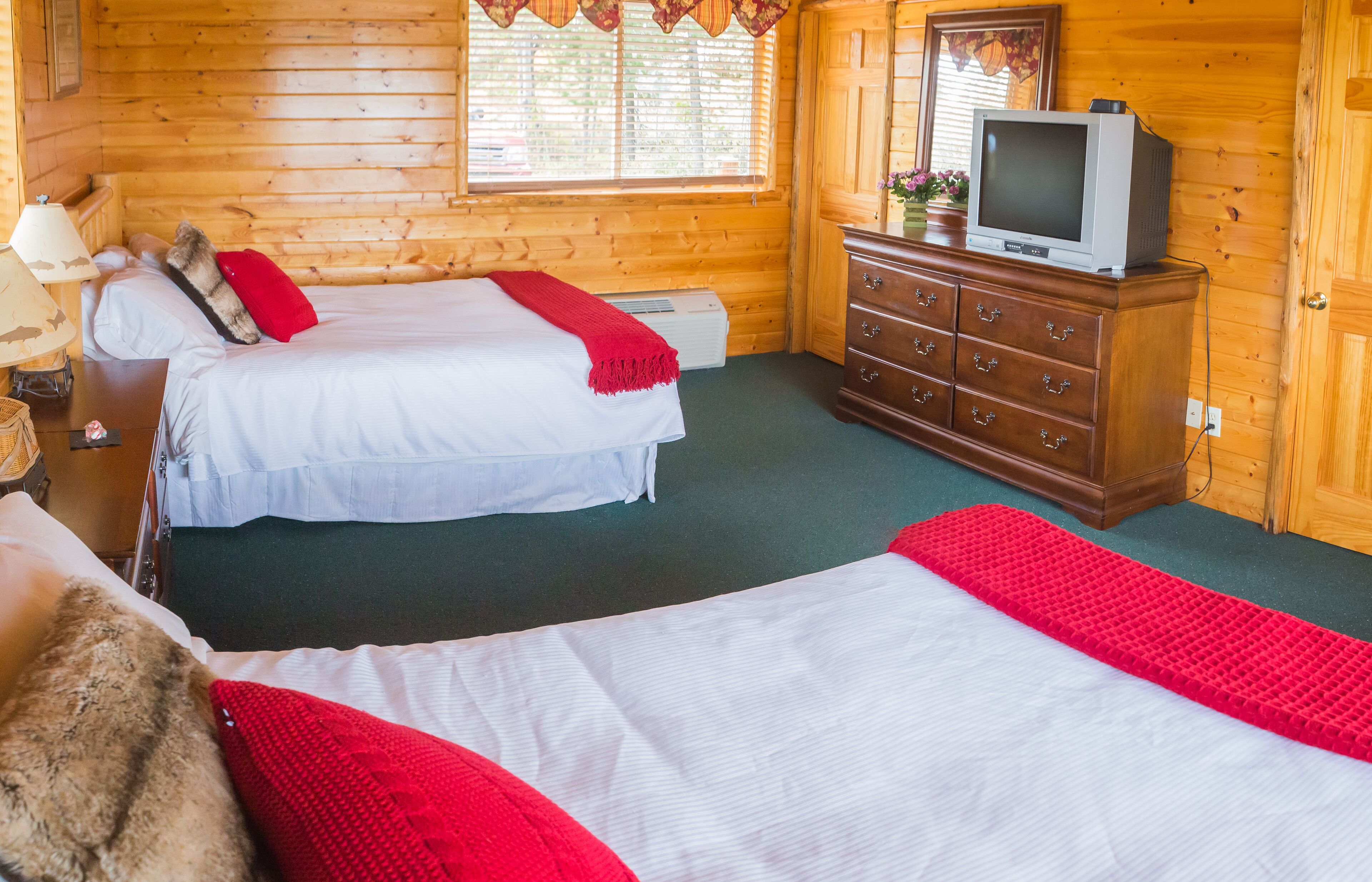 Een kamer in chaletstijl met twee bedden, een dressoir, een televisie en een raam met gordijnen.