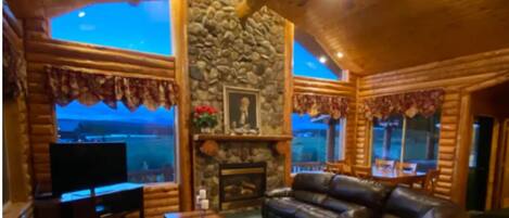 A log cabin interior with a stone fireplace, leather sofa, and a television.