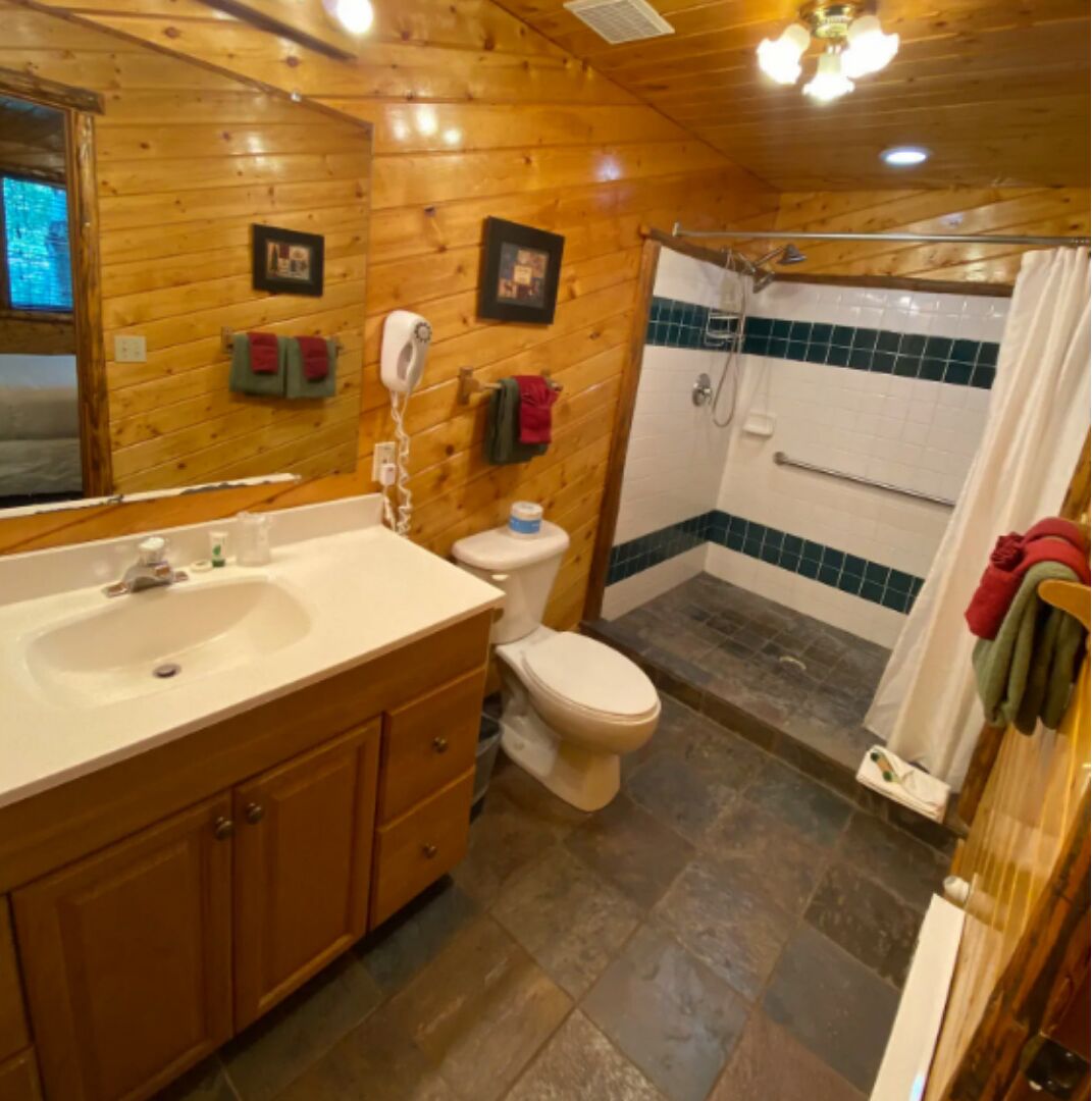 A wooden cabin bathroom with a sink, toilet, and shower.