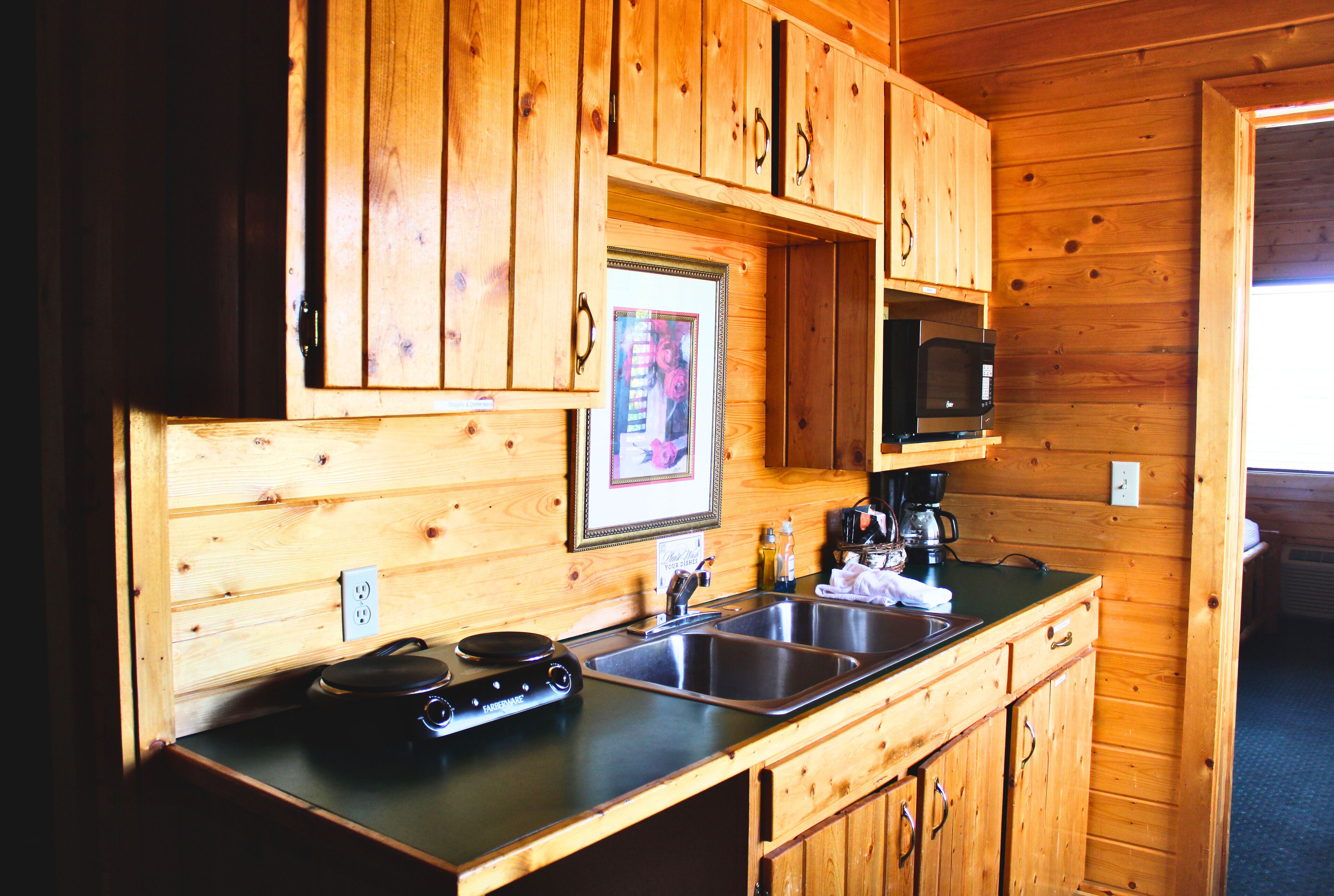 A wooden cabin-style kitchen with a double sink, a microwave, and a coffee maker.