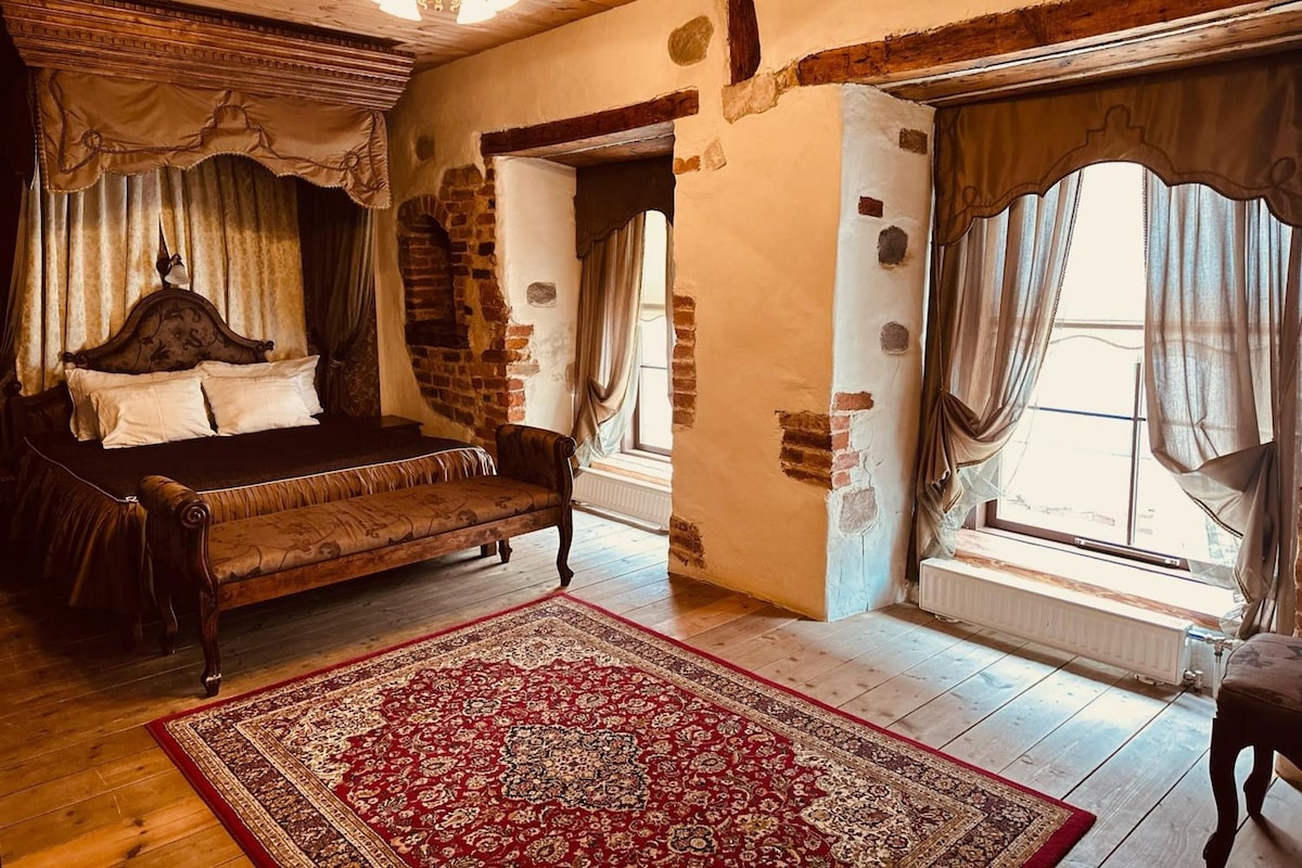 Quarto tradicional com uma cama, um tapete vermelho estampado e teto de madeira.