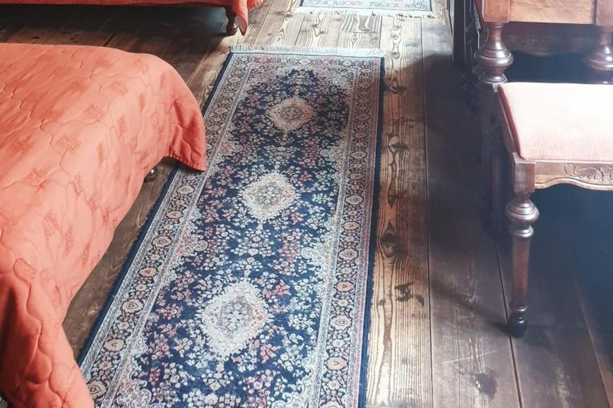 Quarto com duas camas, uma mesa de madeira e um tapete estampado.