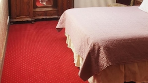 Un dormitorio con techo inclinado, un armario de madera, un radiador, una cama con alfombra roja y un papel tapiz estampado.