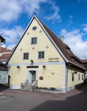 A two-story building with a gabled roof, a central entrance with a small porch, and a sign indicating it is a restaurant and hotel.