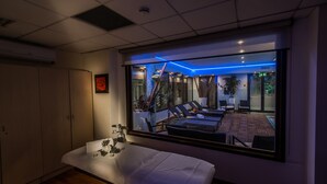 Ein Hotelzimmer mit großem Fenster, einem Bett, einem Nachttisch mit Pflanze und Blick auf den Außenbereich.