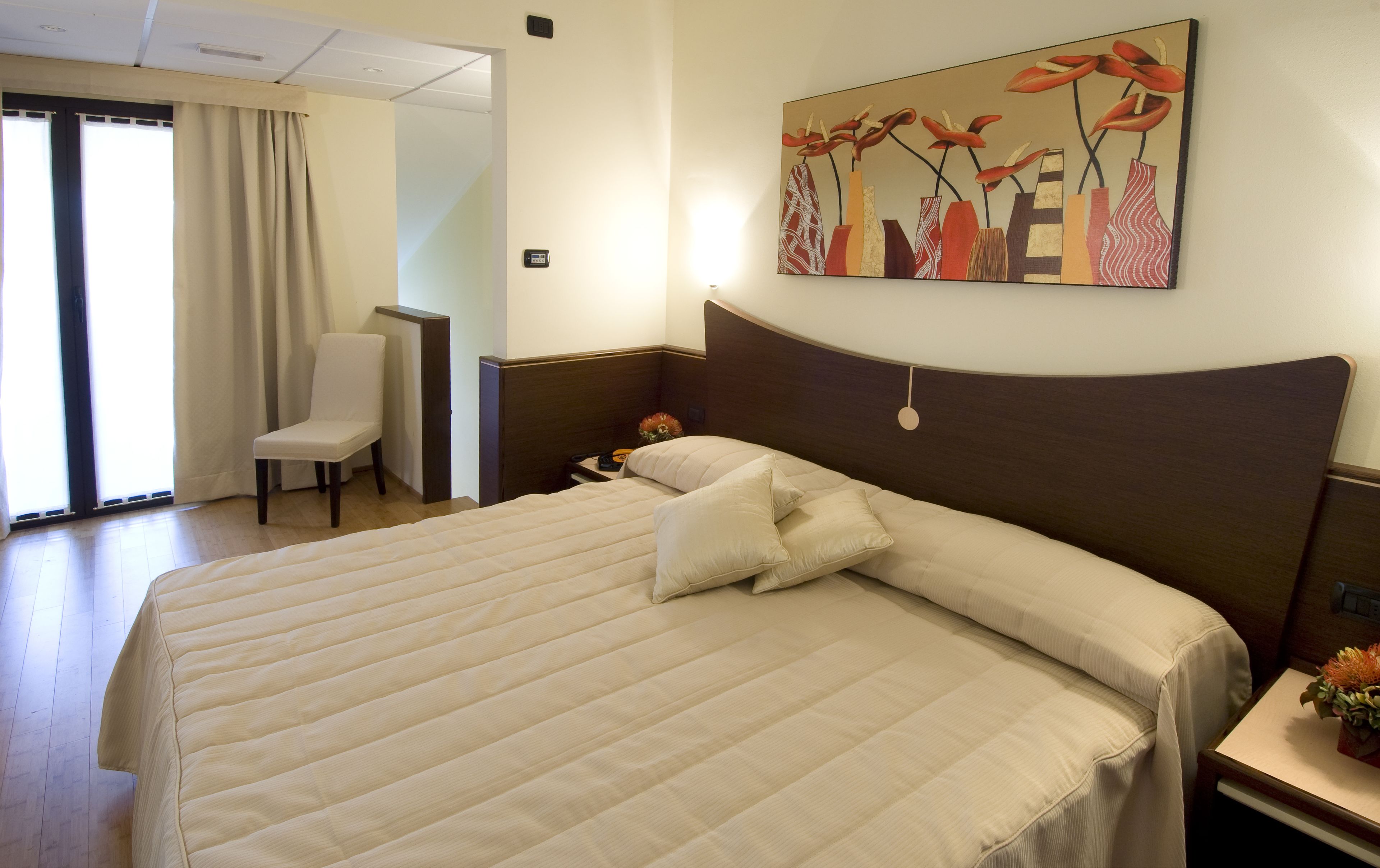 A hotel room with a large bed, a chair, a desk, and a painting on the wall.
