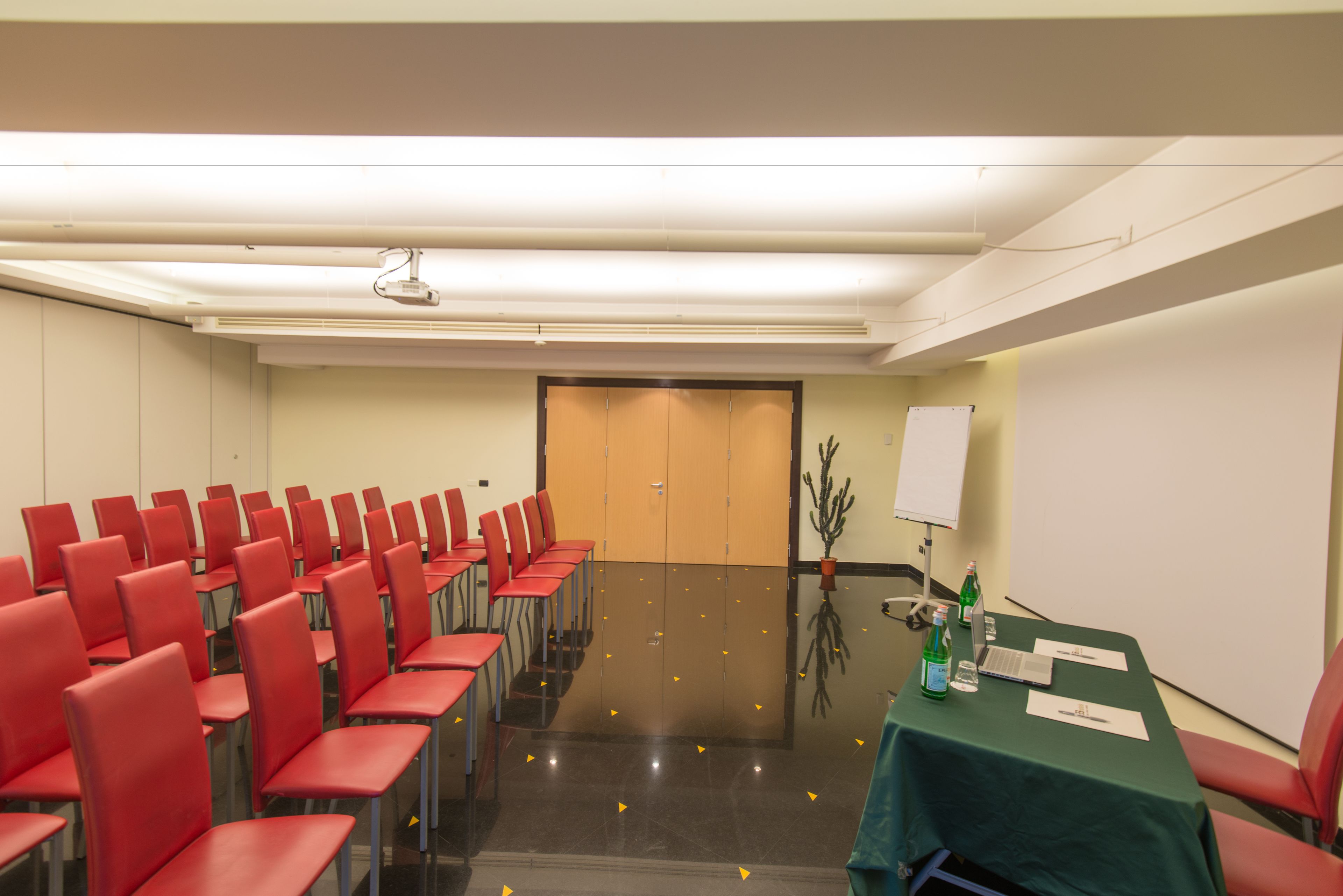 A conference room with rows of red chairs, a table with a green tablecloth, a projector, and a whiteboard.
