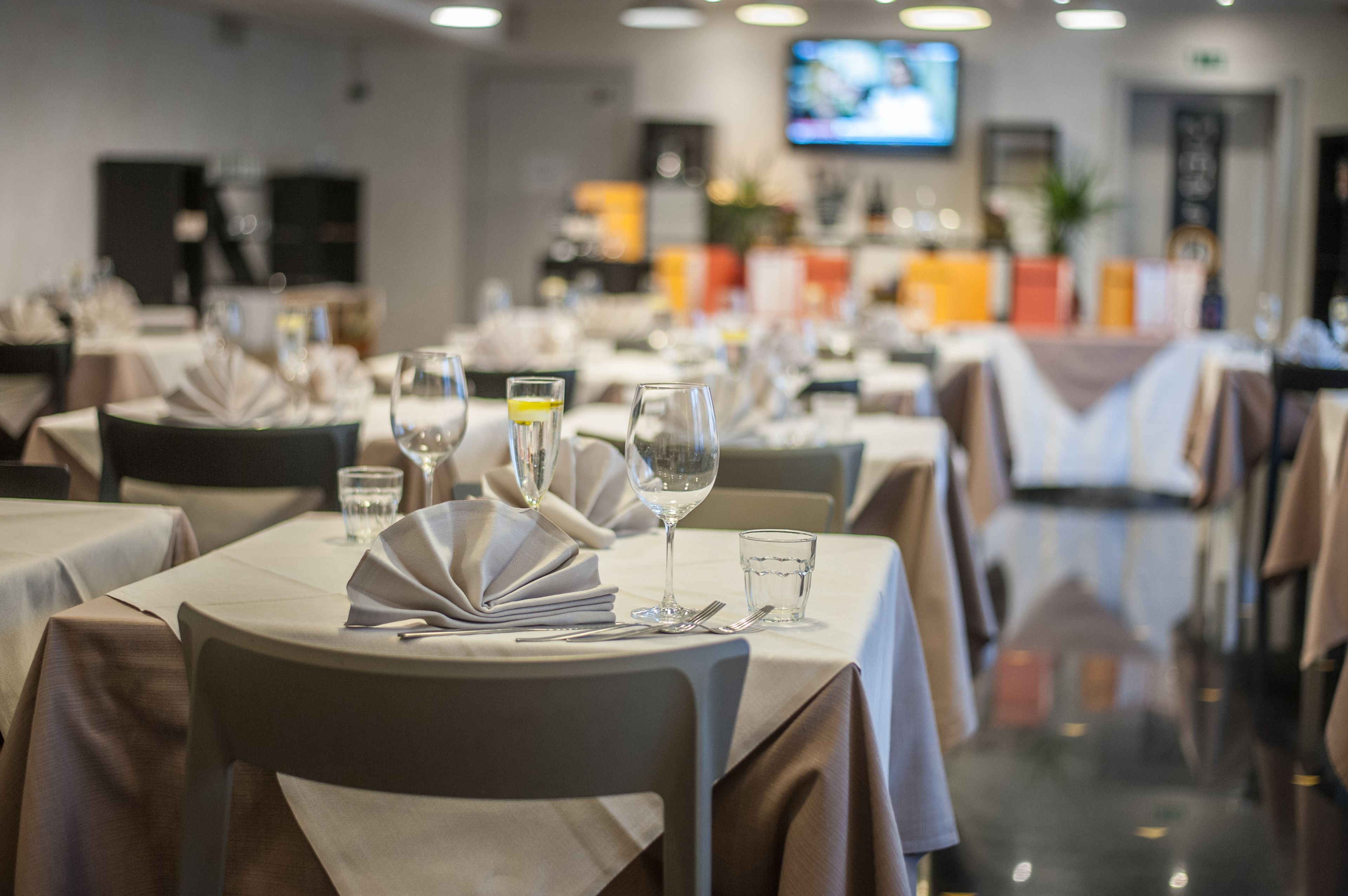 Una sala ristorante con tavoli apparecchiati, inclusi bicchieri e posate.