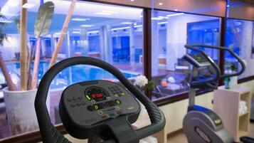 Un gimnasio con equipo de ejercicio, incluyendo una cinta de correr y una máquina de remo, con vista del interior y una ventana al exterior.