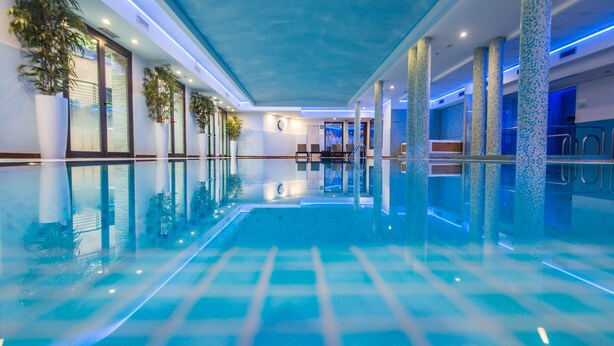 Ein Hallenbad mit klarem Wasser, gefliestem Boden und blauem Licht.