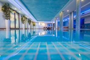 An indoor swimming pool with clear water, tiled flooring, and blue ambient lighting. - AS Hotel Cambiago (Cambiago)