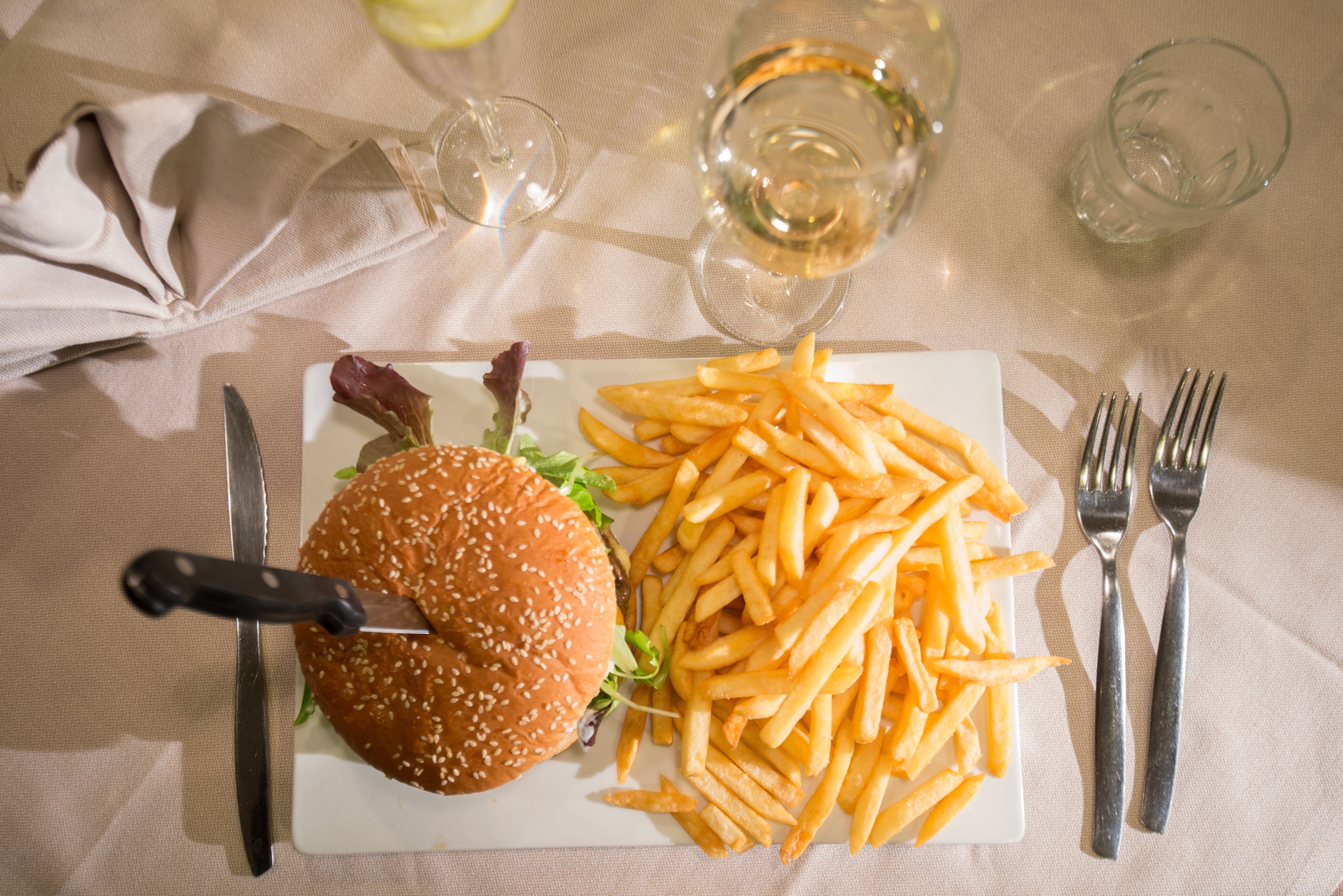 A meal of a hamburger and fries on a white plate, with a knife and fork on the side.
