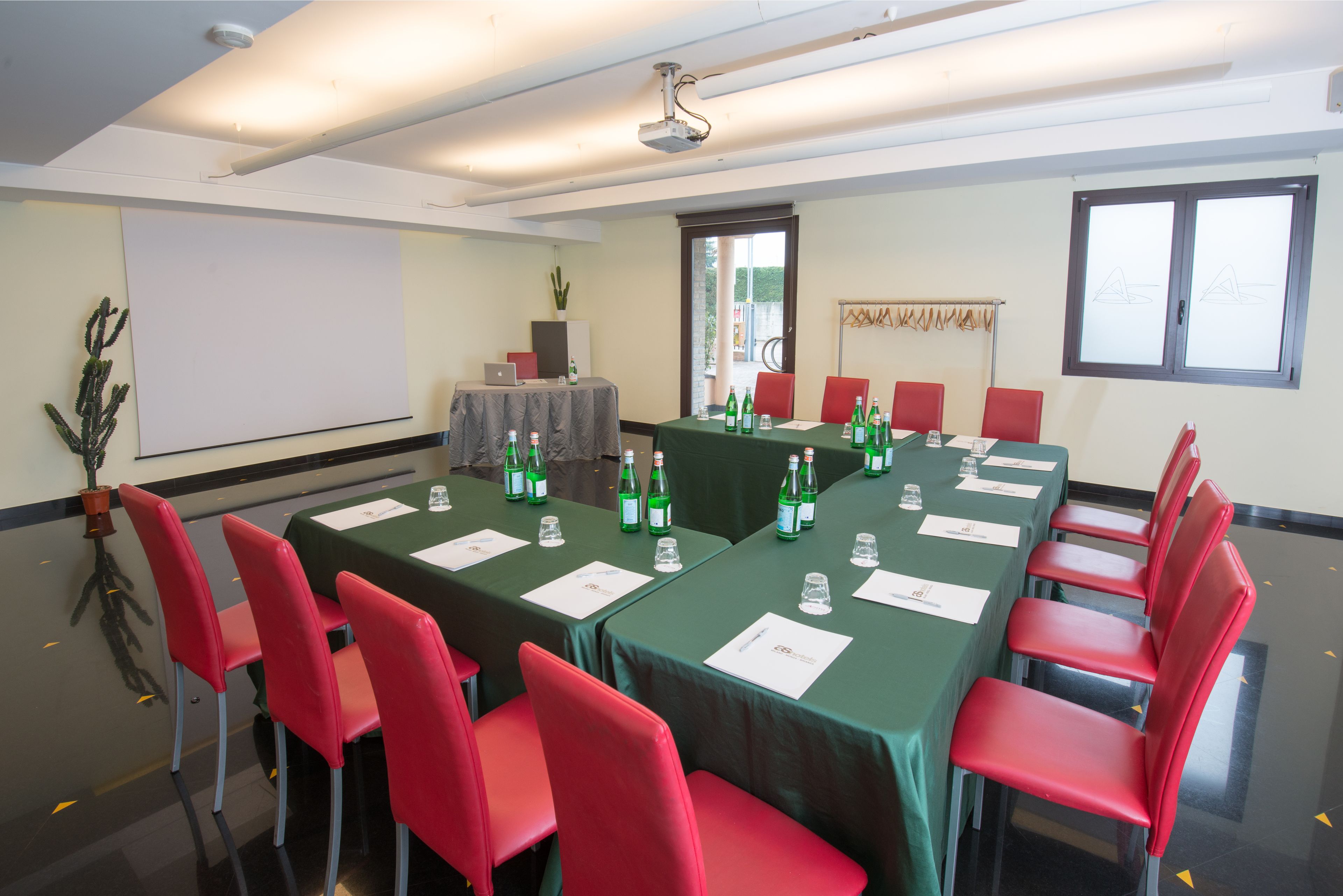 Une salle de conférence avec une longue table, des chaises rouges et des nappes vertes. On y trouve des bouteilles d’eau et des verres sur la table.