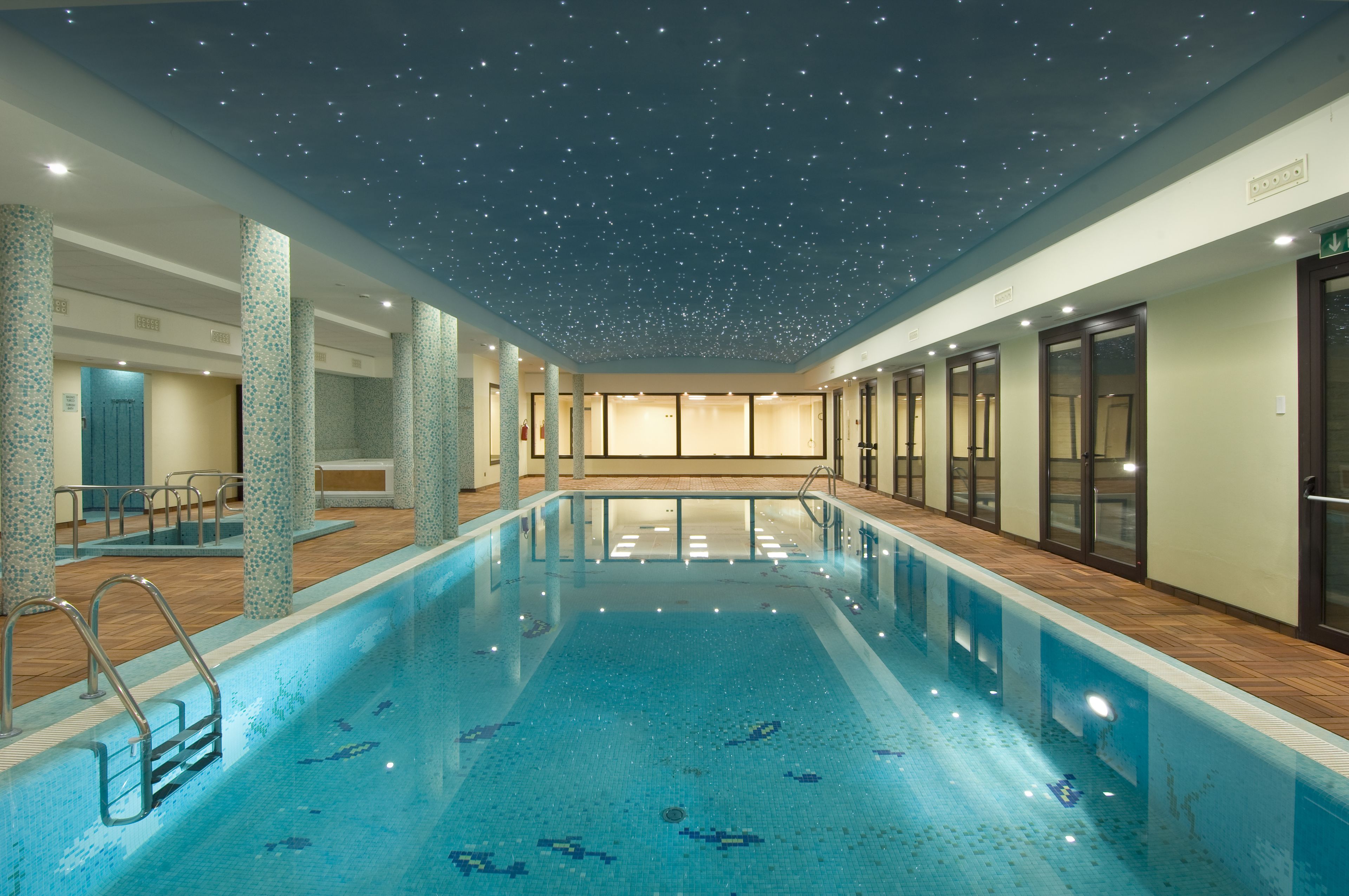 An indoor swimming pool with a starry ceiling, clear poolside area, and adjacent rooms.