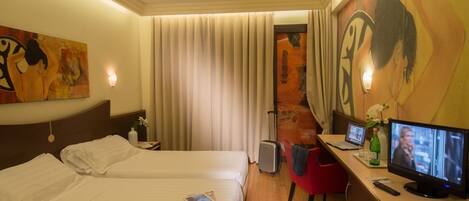 Una habitación de hotel con dos camas, un escritorio con ordenador, un televisor y obras de arte en las paredes.