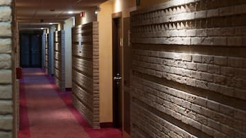 A hotel corridor with a red carpet, brick wall panels, and doors leading to rooms.