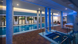 Ein Hallenbad mit Fliesenkolonnen, einer Holzdielen-Terrasse und Liegestühlen.