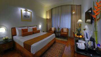 A hotel room with a large bed, a sitting area with a chair and table, a coffee maker, and a TV on the wall.