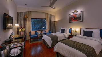 A hotel room with two beds, a desk with a lamp, a chair, and a window with curtains.