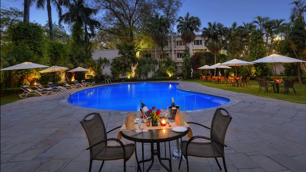 A poolside dining area with a table set for two, surrounded by lounge chairs and umbrellas. - Hotel Clarks (Varanasi)