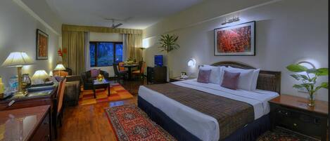 Habitación de hotel con cama, escritorio, silla, lámpara y vistas al exterior.
