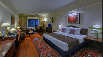 A hotel room with a bed, desk, chair, lamp, and a view of the outdoors.