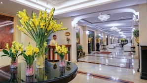 A hotel lobby with a reception desk, a man standing behind it, and a glass table with yellow flowers. - Hotel Clarks (Varanasi)