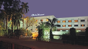 A hotel with a sign reading "Clark Varanasi" at night, surrounded by palm trees and a fenced area. - Hotel Clarks (Varanasi)