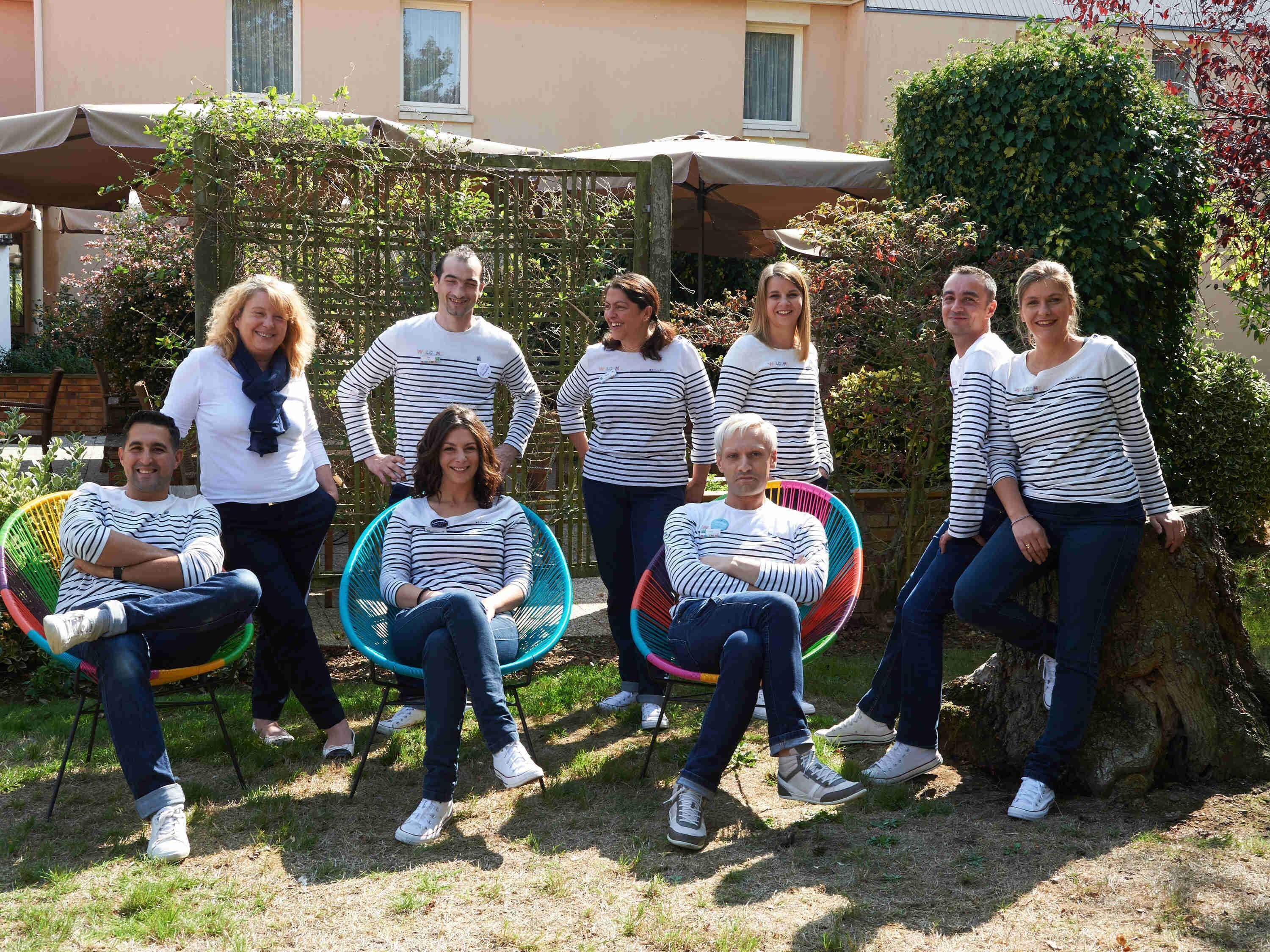 A group of people seated on colorful chairs in an outdoor setting with a building in the background.