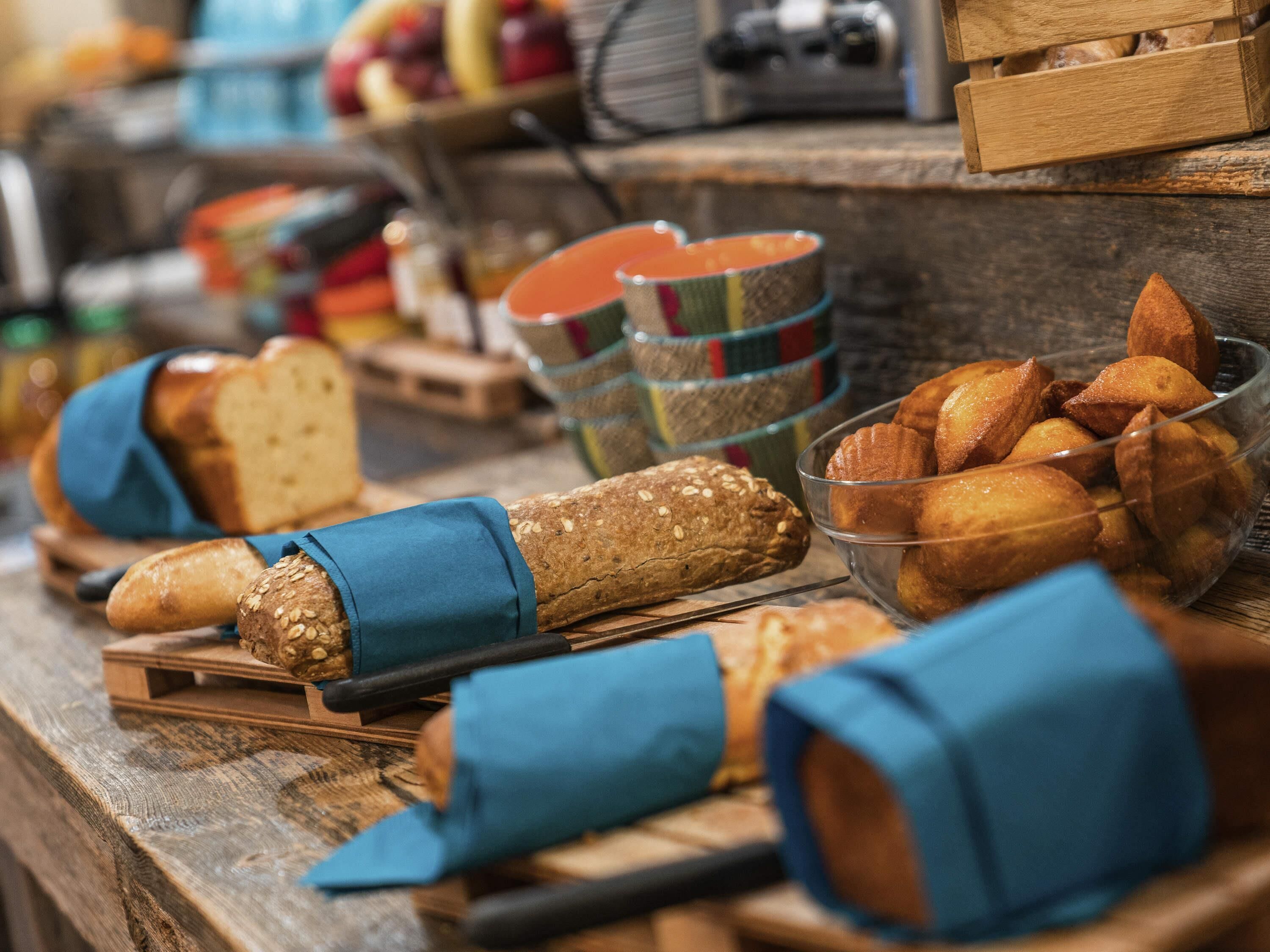 A variety of breads and pastries on a wooden counter, with some wrapped in blue cloth.