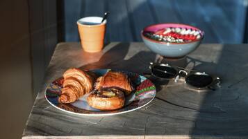 Una mesa con croissants, una taza de café, un bol y gafas de sol.