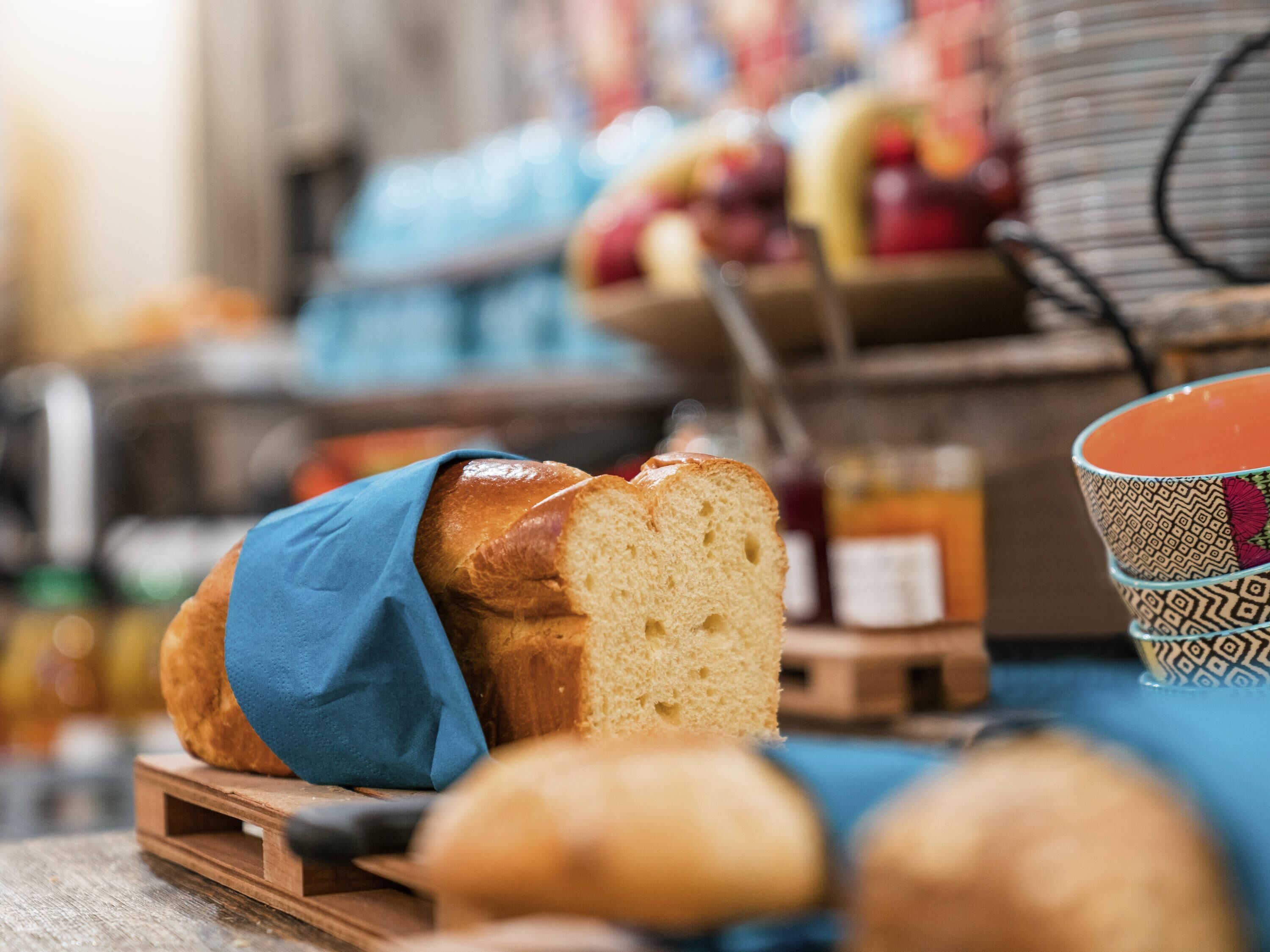 A loaf of bread on a wooden board, with a blue cloth over it.