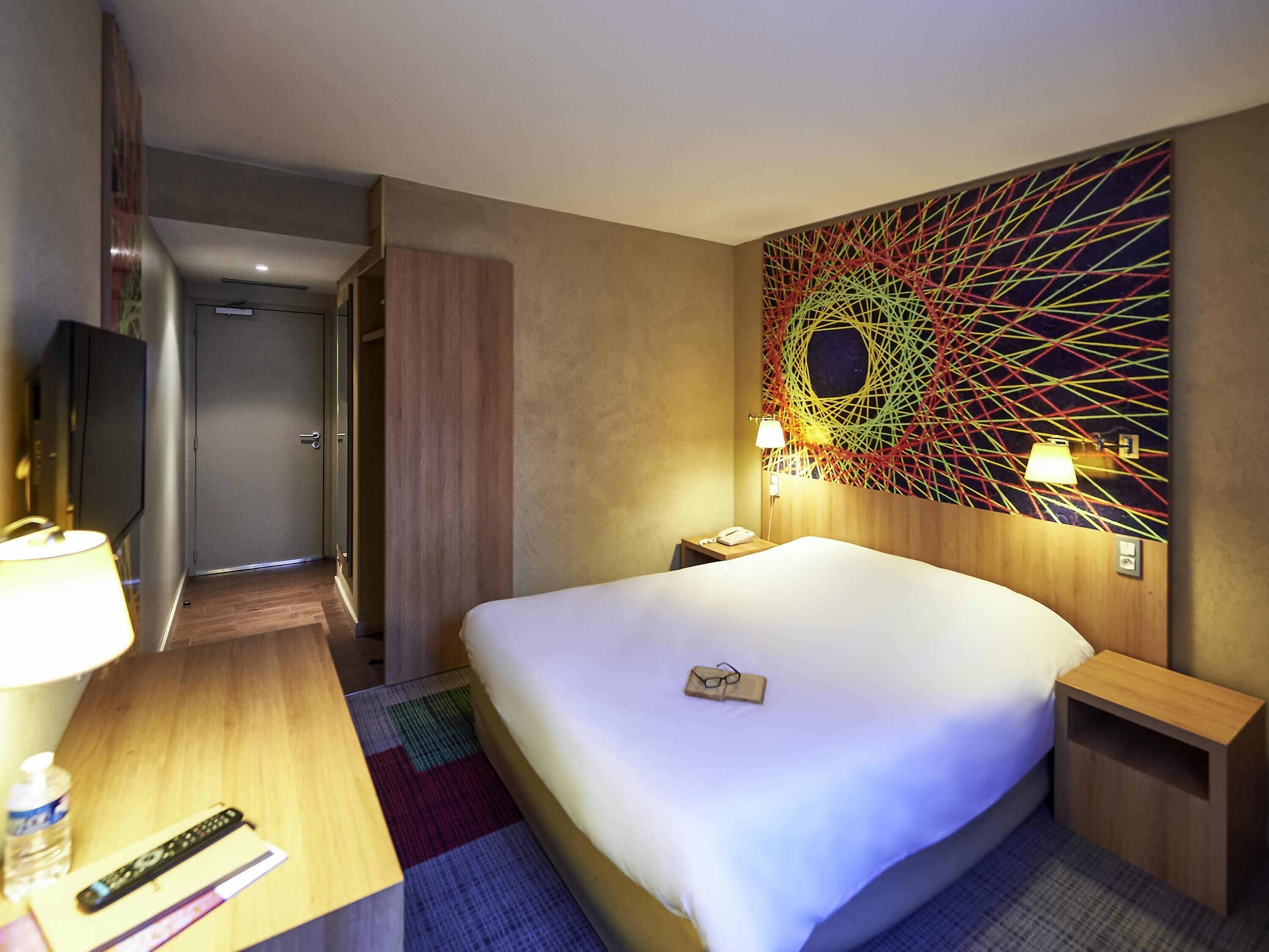 Una habitación de hotel con una cama grande, mesitas de noche, un televisor y una obra de arte en la pared.