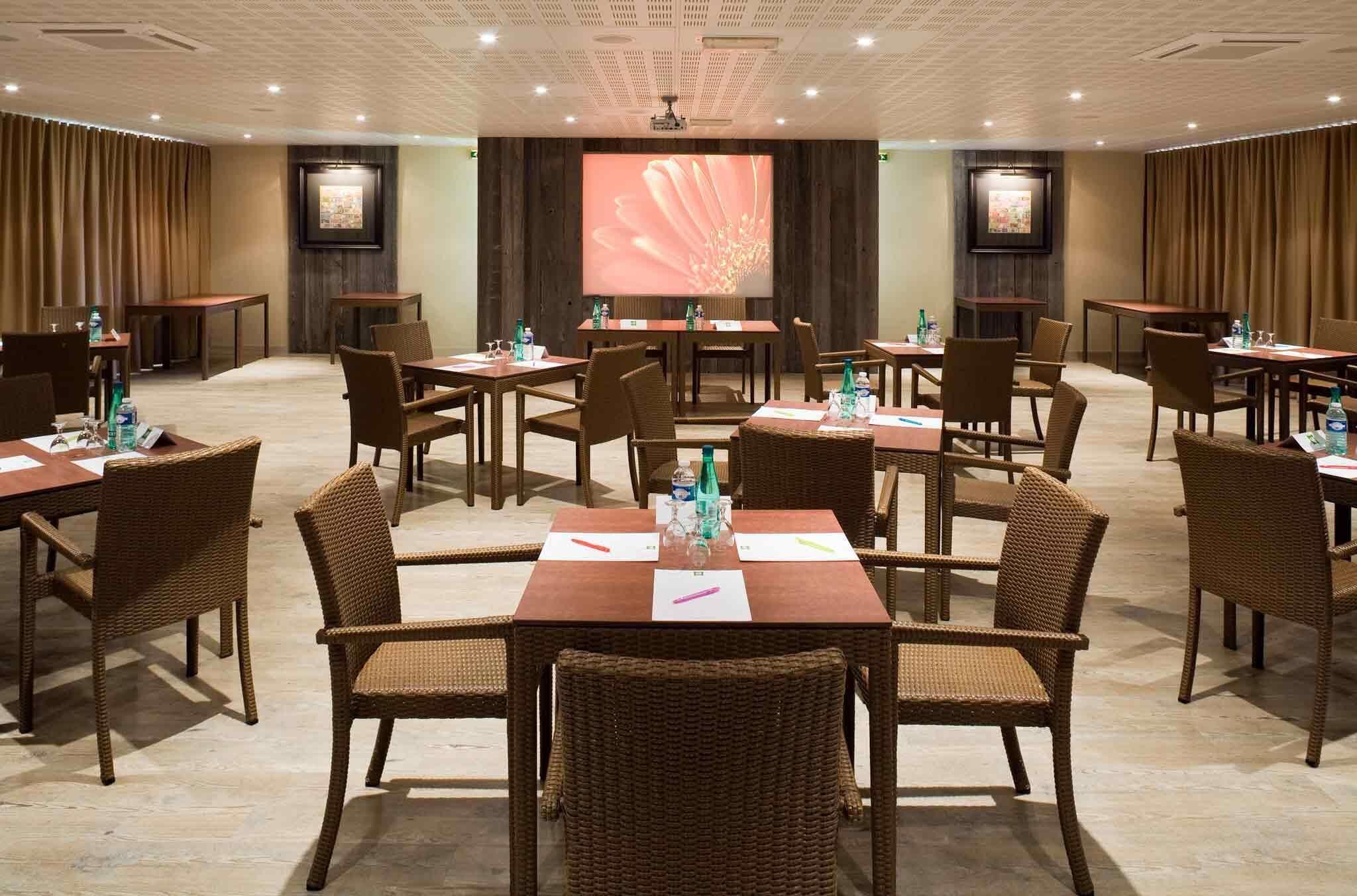 A conference room with multiple tables and chairs, a large screen, and a projector.