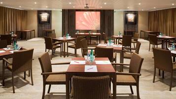 A conference room with multiple tables and chairs, a large screen, and a projector.
