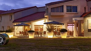 A two-story building with a patio area featuring outdoor seating and umbrellas. - ibis Styles Cholet (Cholet)