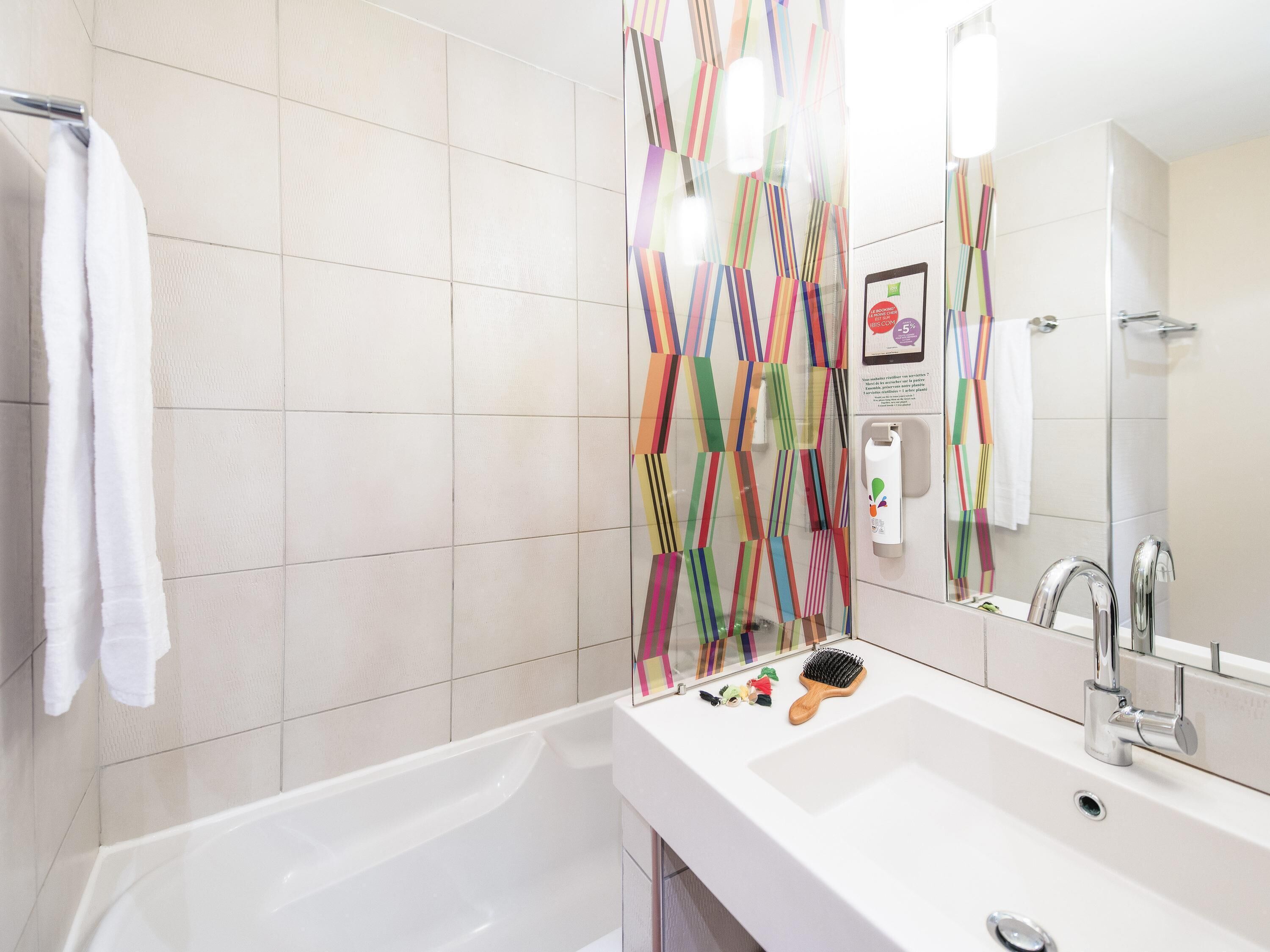A bathroom with a bathtub, a sink, a mirror, and a shower curtain with a colorful geometric pattern.